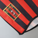 AC Milan Home 99/00 Retro Olympic em destaque, mostrando o logo da Adidas e das listras vermelhas e pretas.