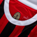 Gola da camisola AC Milan home 24/25 com detalhes em vermelho e preto, símbolo da Puma e histórico do clube.