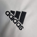 Logo da marca adidas em destaque, bordado em preto sobre tecido claro.