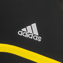 Detalhe da camisola com logo da marca adidas em fundo preto e faixa amarela, representando o Real Madrid.