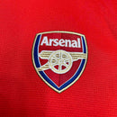 Emblema da camisola Arsenal Home 12/13 da OLYMPIC STORE com fundo vermelho e detalhes dourados.