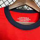 Detalhe da gola da camisola Arsenal Home 12/13, com inscrição "VICTORIA CONCORDIA CRESCIT" em um fundo vermelho.