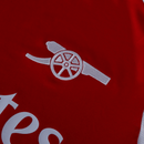 Detalhe do logotipo do Arsenal na camisa vermelha, destacando o canhão do Arsenal home 24/25.