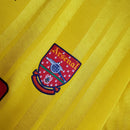 Detalhe do escudo do Arsenal em uniforme amarelo, parte da coleção Arsenal Home 93/94 Retro Olympic Store.