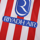 Camisola principal do Atlético de Madrid 2025/26 da Nike, com riscas vermelhas e brancas, gola branca, escudo com contorno amarelo e logótipo azul royal.