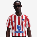 Camisola principal do Atlético de Madrid 2025/26 da Nike, com riscas vermelhas e brancas, gola branca, escudo com contorno amarelo e logótipo azul royal.