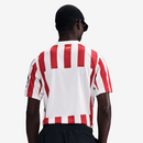 Camisola principal do Atlético de Madrid 2025/26 da Nike, com riscas vermelhas e brancas, gola branca, escudo com contorno amarelo e logótipo azul royal.