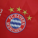Emblema do FC Bayern München em camisa vermelha com quatro estrelas, representando conquistas do clube.