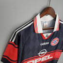 Camisa Bayern München Home 97/98 Retro em exibição, detalhes em vermelho e preto, marca Adidas e logo Opel.