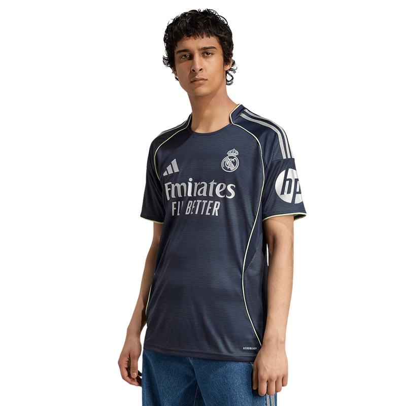 Camisola reserva do Real Madrid 2025/26 da Adidas, em azul-marinho com detalhes prateados e linhas verde fluorescente, sobre fundo branco.
