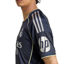Camisola reserva do Real Madrid 2025/26 da Adidas, em azul-marinho com detalhes prateados e linhas verde fluorescente, sobre fundo branco.