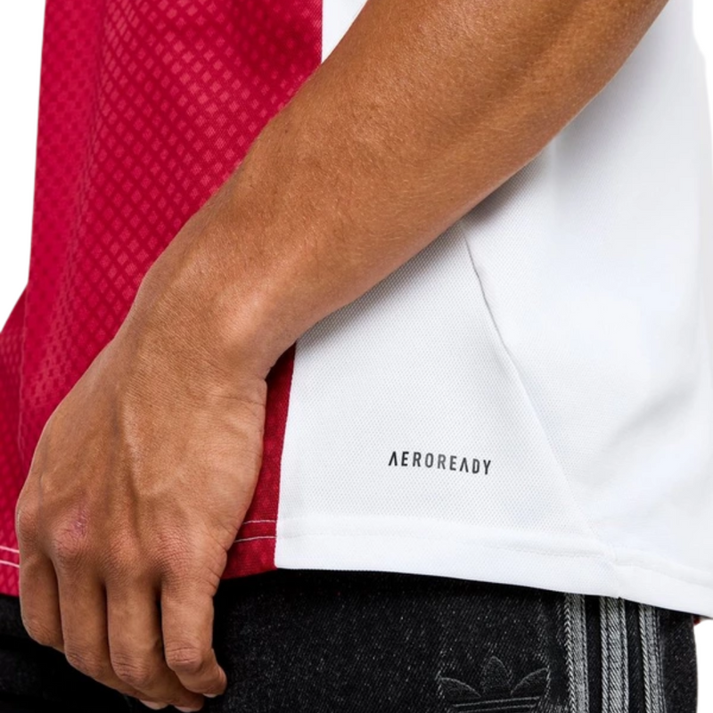 Camisola principal do Ajax 2025/26 Adidas em branco e vermelho com faixa central em padrão gradiente, gola em V e detalhes icónicos da cidade de Amesterdão.