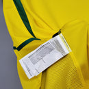 Camisola Brasil Home 2002 Retro com detalhes em amarelo e etiqueta de cuidados visível.