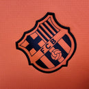 Logotipo da camisola FC Barcelona third laranja 2025/26 - TOTAL 90, destacando o emblema do time.