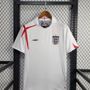 Camisola Inglaterra home 2005 Retro exposta em um cabide sobre uma grade de metal.