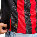 Camisola principal do AC Milan 2025/26 com riscas vermelhas e pretas estilizadas em forma de chamas, gola preta e escudo em vermelho e branco