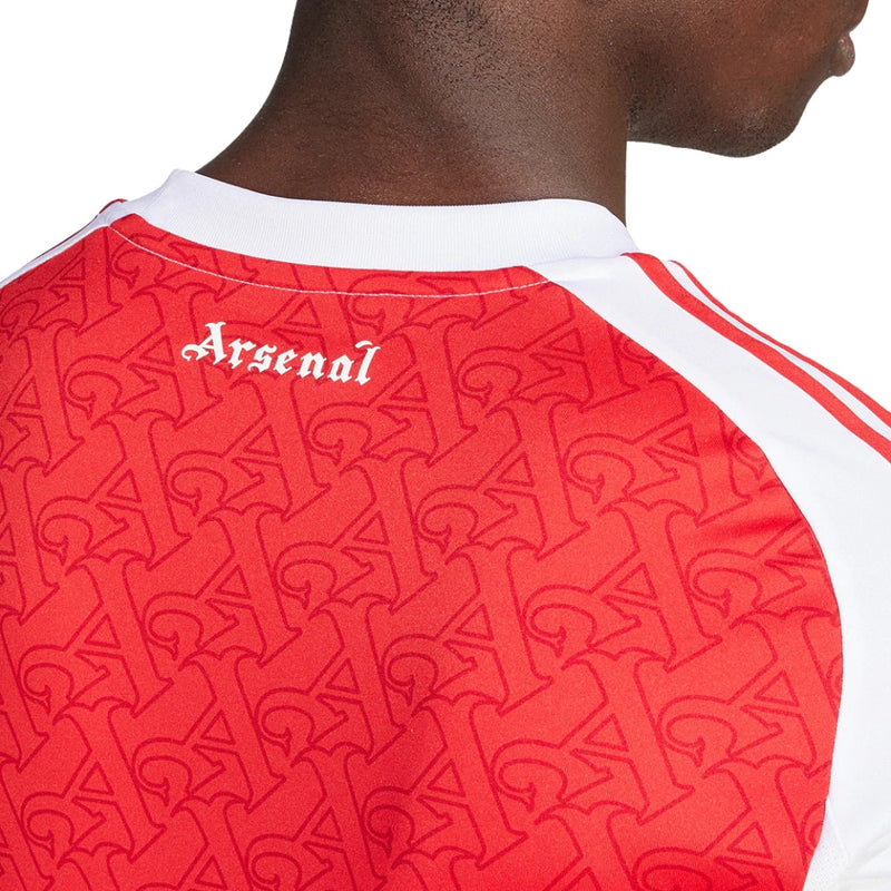 Camisola principal do Arsenal 2025/26 da Adidas, em vermelho com mangas brancas e padrão gótico subtil com a letra “A”, gola redonda e logos em branco.