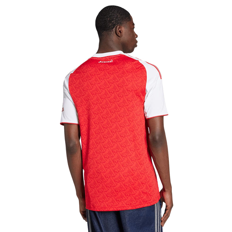 Camisola principal do Arsenal 2025/26 da Adidas, em vermelho com mangas brancas e padrão gótico subtil com a letra “A”, gola redonda e logos em branco.