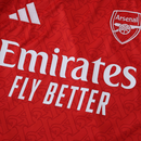 Camisola principal do Arsenal 2025/26 da Adidas, em vermelho com mangas brancas e padrão gótico subtil com a letra “A”, gola redonda e logos em branco.