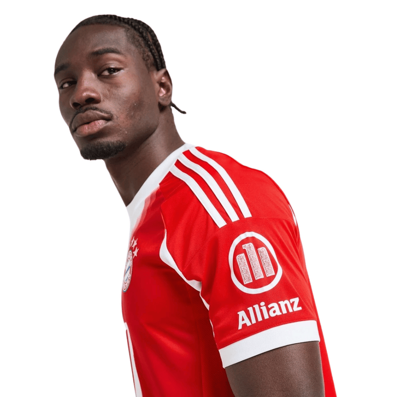 Camisola oficial do Bayern de Munique 2025–2026 em vermelho com detalhes brancos, escudo do clube e lema “Mia San Mia” bordado na parte de trás da gola.