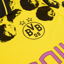 Camisola principal amarela e preta do Borussia Dortmund 2025 com padrão hexagonal nos ombros e detalhes artísticos pintados à mão, colaboração Puma x KidSuper.