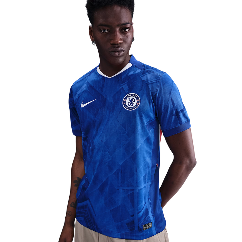 Camisola principal do Chelsea 2025/26 da Nike em azul royal com estampado gráfico inspirado em Londres, gola em V branca e detalhes em vermelho e branco.