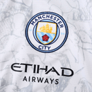 Camisola branca do Manchester City 25/26 com faixa diagonal preta e vermelha, padrão Poznań e detalhes artísticos da colaboração KidSuper x Puma
