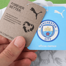 Camisola branca do Manchester City 25/26 com faixa diagonal preta e vermelha, padrão Poznań e detalhes artísticos da colaboração KidSuper x Puma