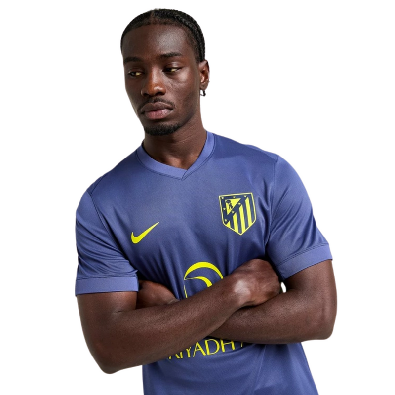 Camisola secundária do Atlético de Madrid 2025/26 da Nike em roxo com raios amarelos e selo “ATLETI – Not Turning Back” na gola, vista frontal.
