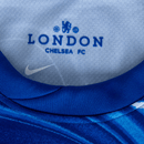 Detalhe do colarinho da camisa Chelsea home 24/25 Azul Olympic com logo e nome Chelsea FC.