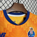 Conjunto infantil FC Porto laranja alternativo 2024/25 exposto em cabide, detalhe do acabamento e logo.