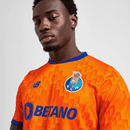 Modelo usando a camisola FC Porto away 24/25 Laranja, destacando o logo do clube e a marca New Balance.