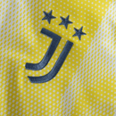 Detalhe do bordado da camisolas Juventus away 24/25 amarelo com logo da equipe e estrelas acima.