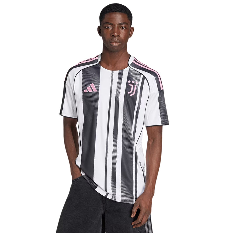 Camisola principal da Juventus 2025/26 da Adidas, com riscas pretas e brancas irregulares, gola TEAMGEIST, e detalhes em rosa no escudo e logos.