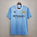 Camisa retrô do Manchester City Home 11/12 com cores azuis e detalhes da marca Umbro.