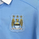 Escudo do Manchester City Home 15/16 Retro em camisa azul, exibindo as estrelas acima e a sigla M.C.F.C.