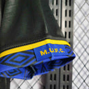 Detalhe da camiseta retro Manchester United Away 93/95 mostrando o logo M.U.F.C. e design icônico em azul e amarelo.
