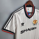 Camisa Manchester United Away 1983 Retro com detalhes em preto e vermelho, fabricada pela Adidas.