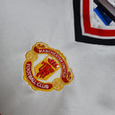 Emblema do Manchester United em camisa retro de 1985, detalhando o famoso logo do clube.