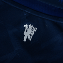 Emblema da camisa azul do Manchester United para a temporada 24/25, destacando o design e a cor.
