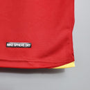 Detalhe da camiseta retro Manchester United Home 06/07 com logo Nike Sphere Dry em fundo vermelho.