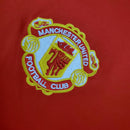 Logo do Manchester United, clube de futebol icônico, na camisa vermelha do time.