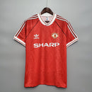 Camiseta retrô Manchester United Home 90/92 com logo Adidas e patrocinador Sharp, fundo cinza.