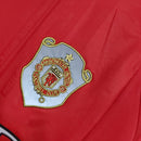 Emblema do Manchester United em camisa retro 99/00, destacando o estilo clássico do time.