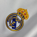 Emblema do Real Madrid na camisola branca 19/20 retro, com detalhes em azul e amarelo.