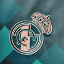 Emblema da camisola do Real Madrid, com detalhes em azul e rosa, simbolizando o clube de futebol.